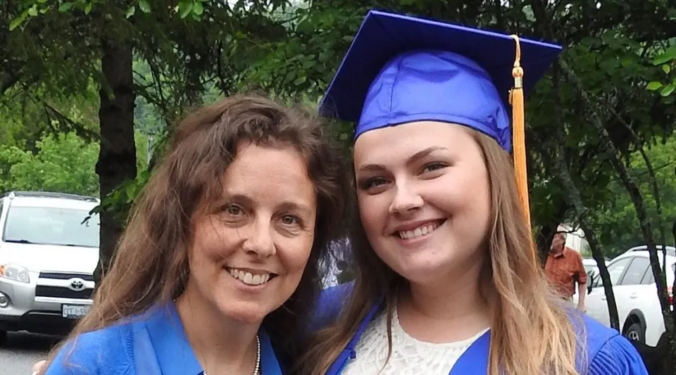 Due donne, una con il tocco da diplomata, sono insieme davanti a uno sfondo boscoso nel campus della Huntsville High School.