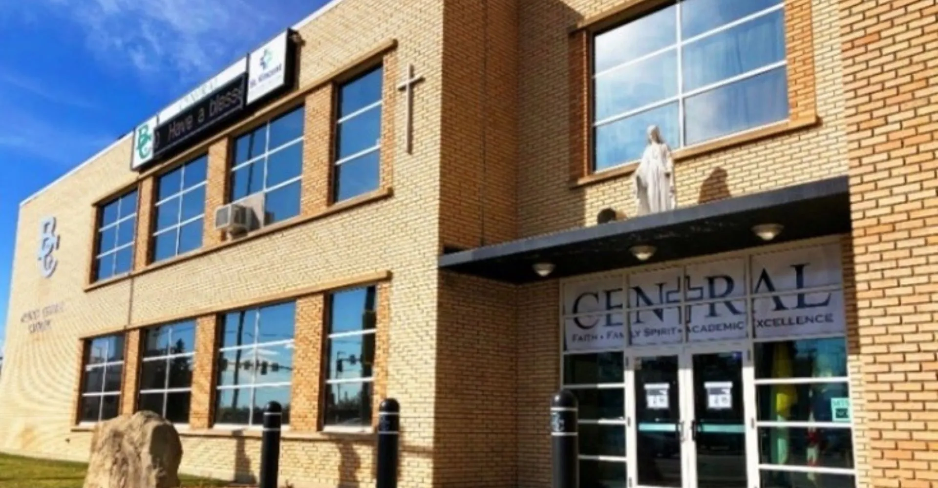 L'edificio in mattoni a più piani della Billings Central Catholic High School con grandi finestre e una scritta ben visibile si staglia contro il cielo blu.