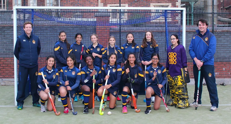Un gruppo di giovani atlete posa sul campo sportivo della Royal School Wolverhampton davanti a un edificio in mattoni.