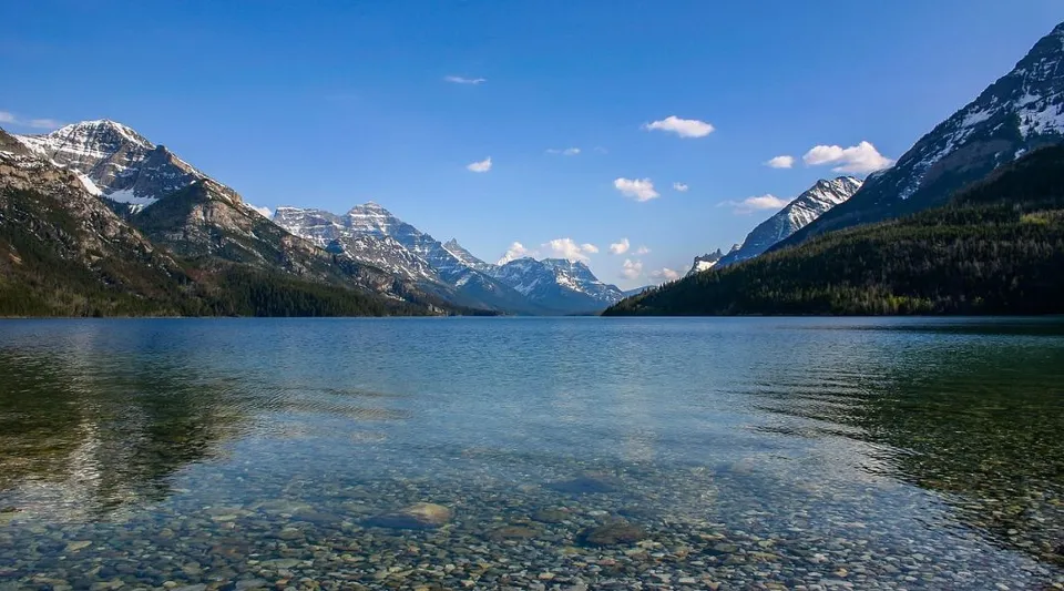 Un lago alpino con una superficie liscia come uno specchio e montagne innevate sullo sfondo vicino alla Warburg School.