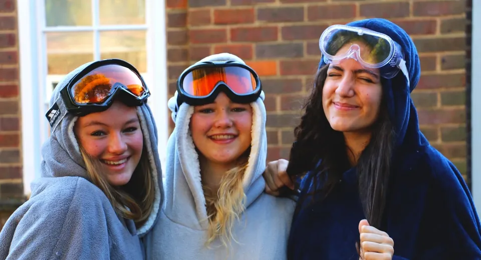 Tre studentesse della The Royal Masonic School for Girls sorridono davanti a un muro di mattoni.