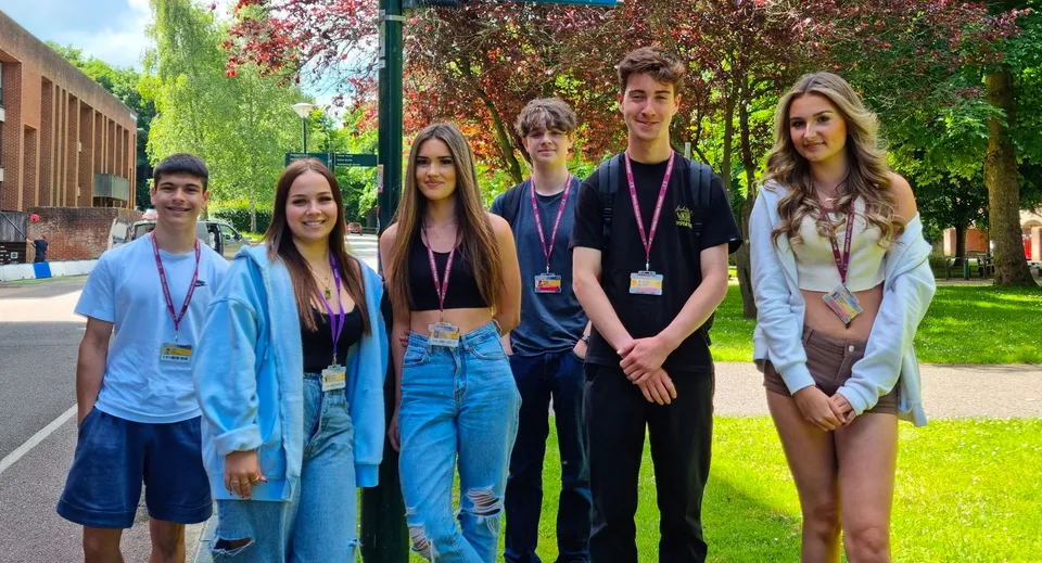 Studenti del Bexhill College sono insieme in un'area simile a un parco con alberi ed edifici sullo sfondo.