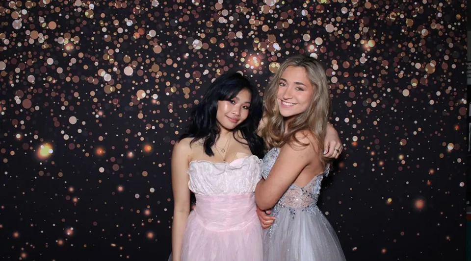 Due studentesse della Forest Ridge School of the Sacred Heart sono in piedi insieme davanti a luci scintillanti durante un evento festivo.
