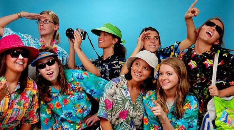 Un gruppo di giovani donne vestite con abiti colorati posa davanti a uno sfondo blu nel campus dell'Aden Bowman Collegiate.