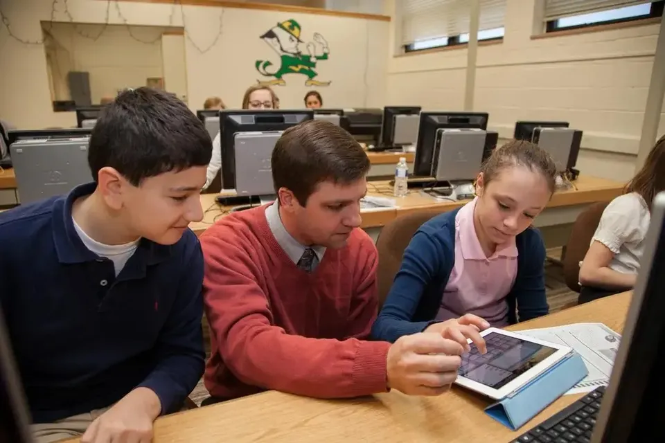 Un insegnante della Regis High School mostra l'uso di un tablet a due studenti in un'aula di informatica.