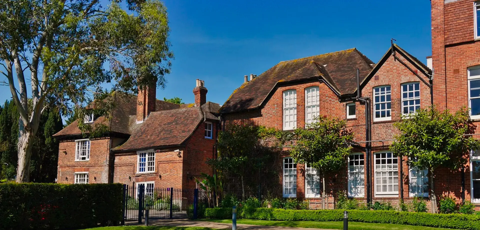 L'edificio in mattoni della Ashford School con tetto in paglia si erge circondato da aree verdi sotto un cielo limpido.