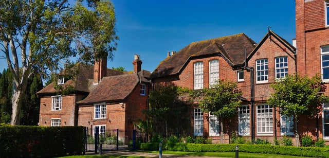 L'edificio in mattoni della Ashford School con tetto in paglia si erge circondato da aree verdi sotto un cielo limpido.
