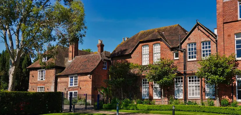 L'edificio in mattoni della Ashford School con tetto in paglia si erge circondato da aree verdi sotto un cielo limpido.