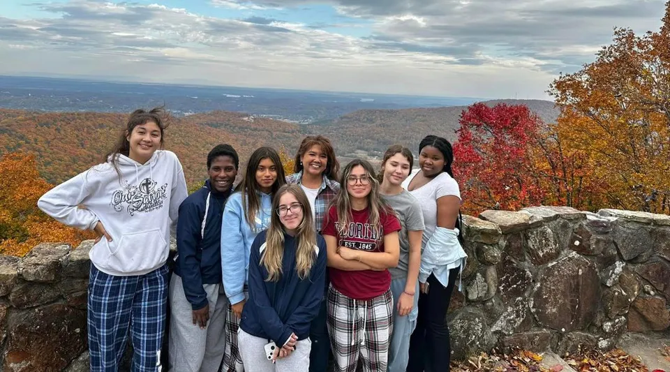 Un gruppo di studenti della Our Savior New American School si trova su una roccia con vista su un variopinto paesaggio autunnale.