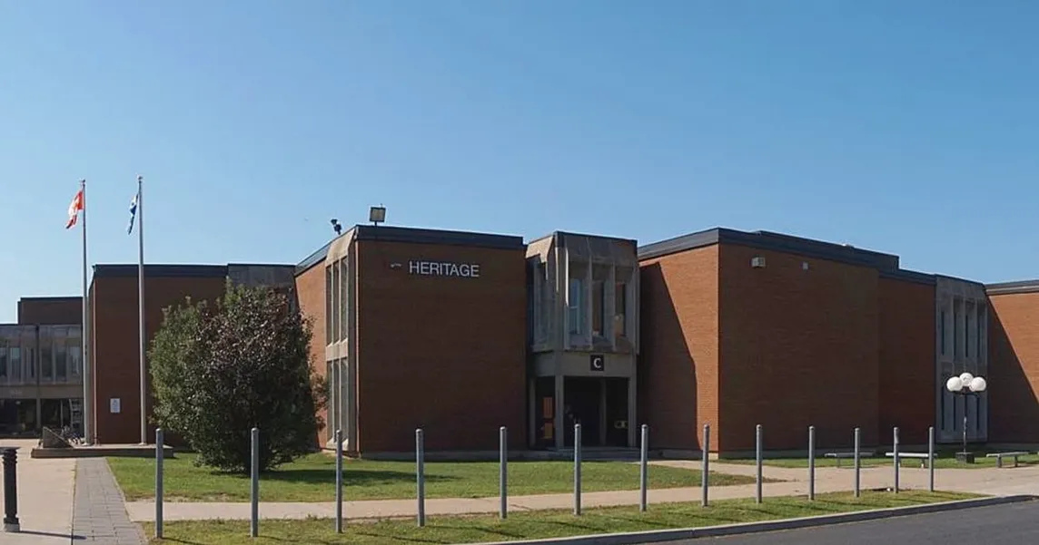 Backsteingebäude einer Schule mit Schriftzug Heritage, davor Fahnenmasten mit kanadischer und Québecer Flagge