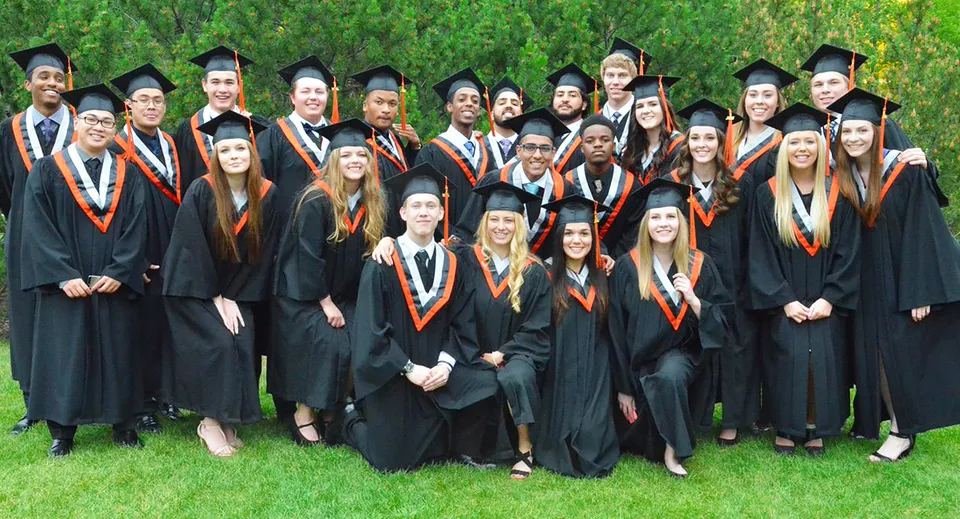 Un gruppo di diplomati della M.E. LaZerte Composite High School si trova su un prato immerso nel verde indossando il tocco e la toga accademica.