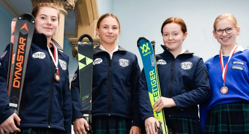 Quattro studentesse della Kingsley School sono in piedi con l'attrezzatura da sci in un centro di allenamento.