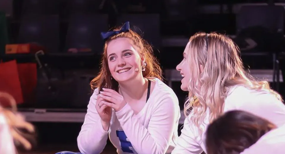 Due studentesse della Papanui High School si trovano insieme su un palco davanti a un sipario scuro.