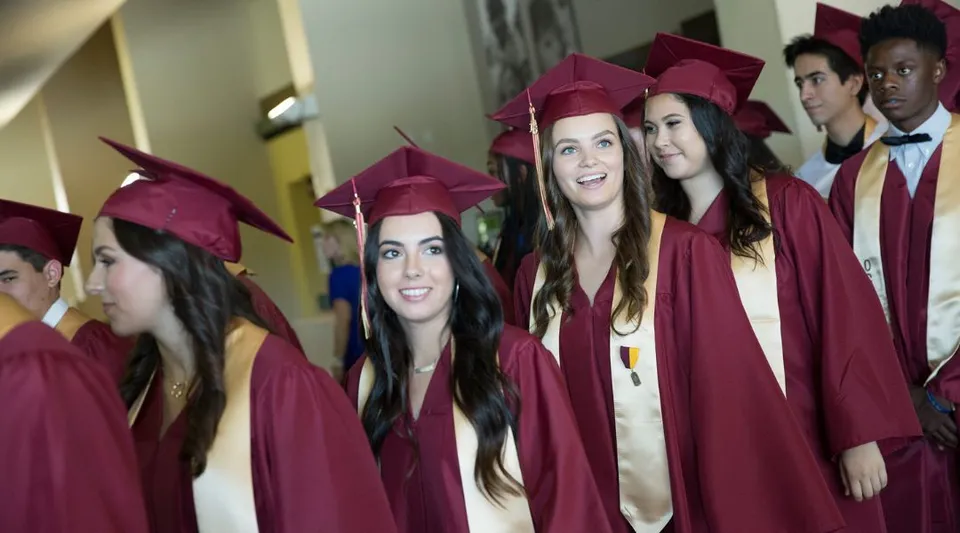 Un gruppo di diplomati della Oaks Christian School in toga rossa festeggia il proprio diploma insieme nel corridoio.