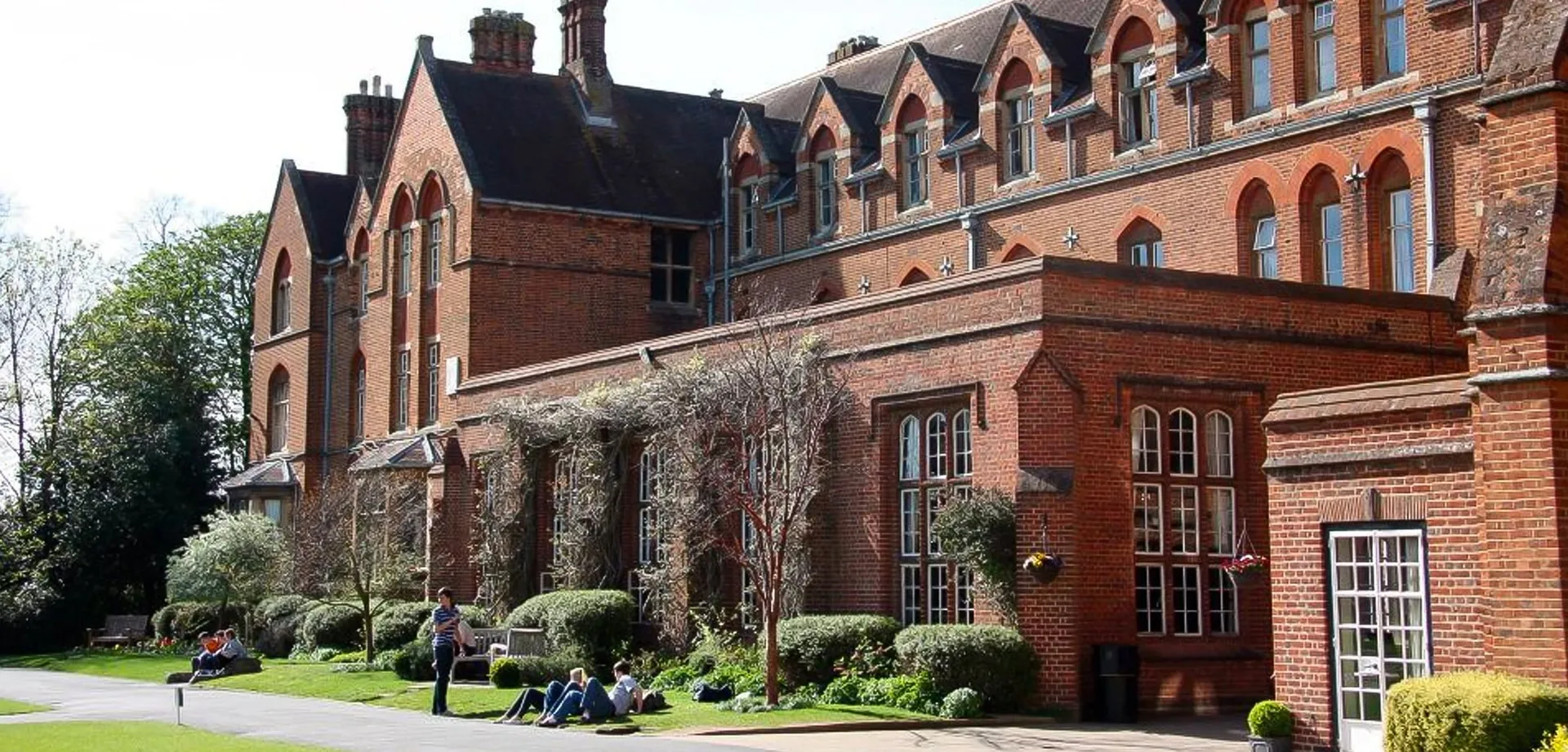 Alcuni studenti siedono sul prato davanti all'edificio in mattoni rossi dell'Oxford International College.