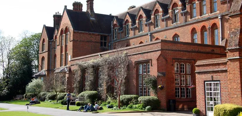Alcuni studenti siedono sul prato davanti all'edificio in mattoni rossi dell'Oxford International College.