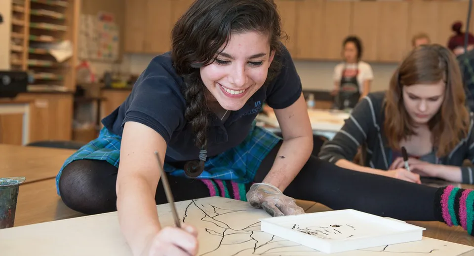 Una studentessa della Argyle Secondary School siede concentrata al tavolo e disegna.