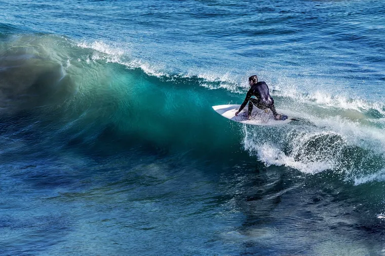 Surfer im Neoprenanzug reitet auf einer türkisblauen Welle