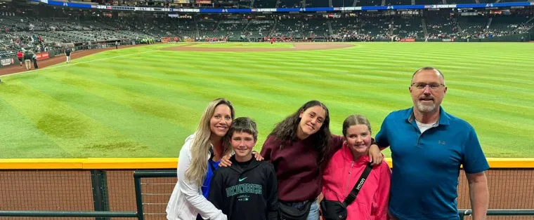 Host family americana con tre ragazzi sorridenti sugli spalti di uno stadio di baseball