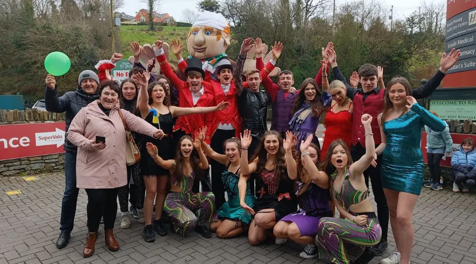 Un gruppo di studentesse della Kinsale Community School posa all'aperto davanti ad alberi ed edifici in abiti da festa colorati.