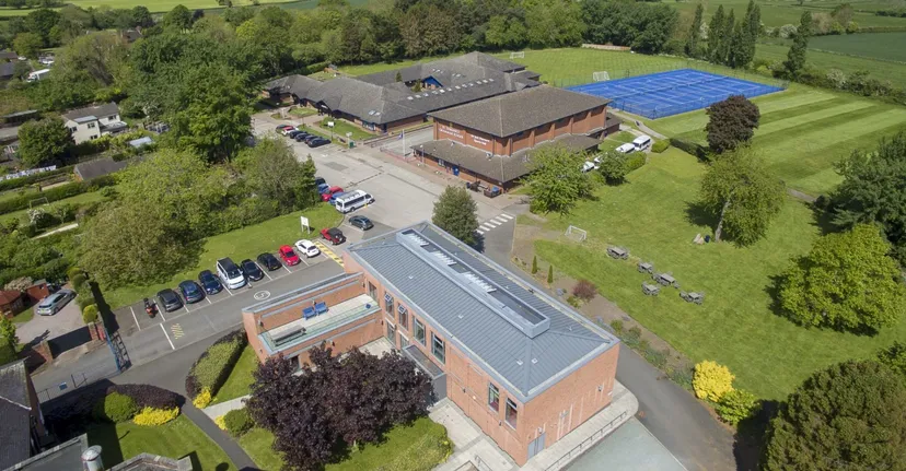 L'edificio in mattoni a più piani della St. Dominic's Grammar School con un impianto solare blu sul tetto sorge su un prato circondato da alberi.