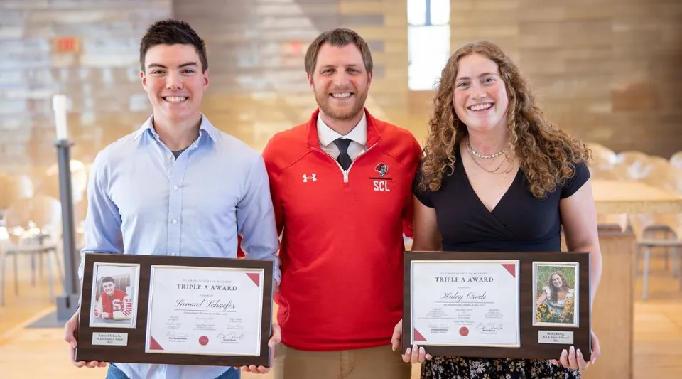 Tre persone tengono degli attestati durante una premiazione nel campus della St. Croix Lutheran Academy.