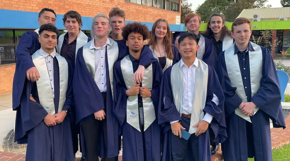 Un gruppo di studenti del Kiara College in toga da diploma posa davanti a un edificio in mattoni.