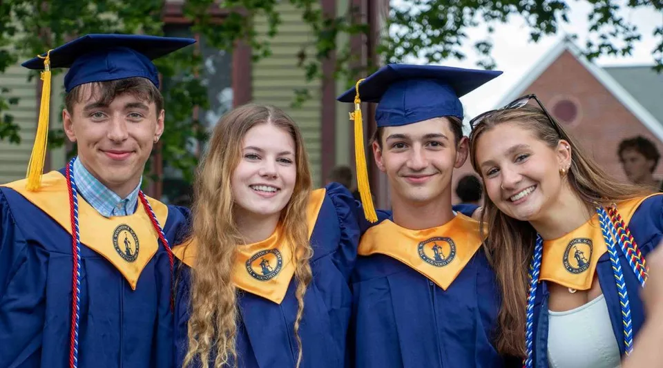 Quattro studenti in toga da diploma posano insieme davanti a un edificio del campus della Woodstock Academy.