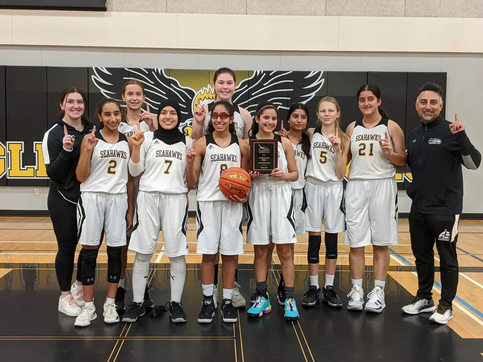 Un gruppo di giocatrici di basket della Seaquam Secondary School tiene una coppa nella palestra.