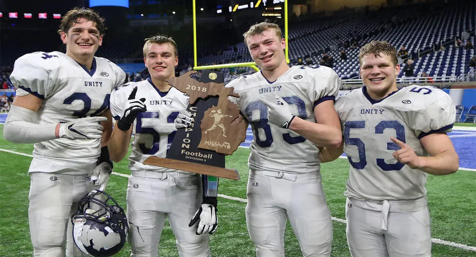 Quattro giocatori di calcio della Unity Christian High School tengono un trofeo sul campo di gioco di notte.