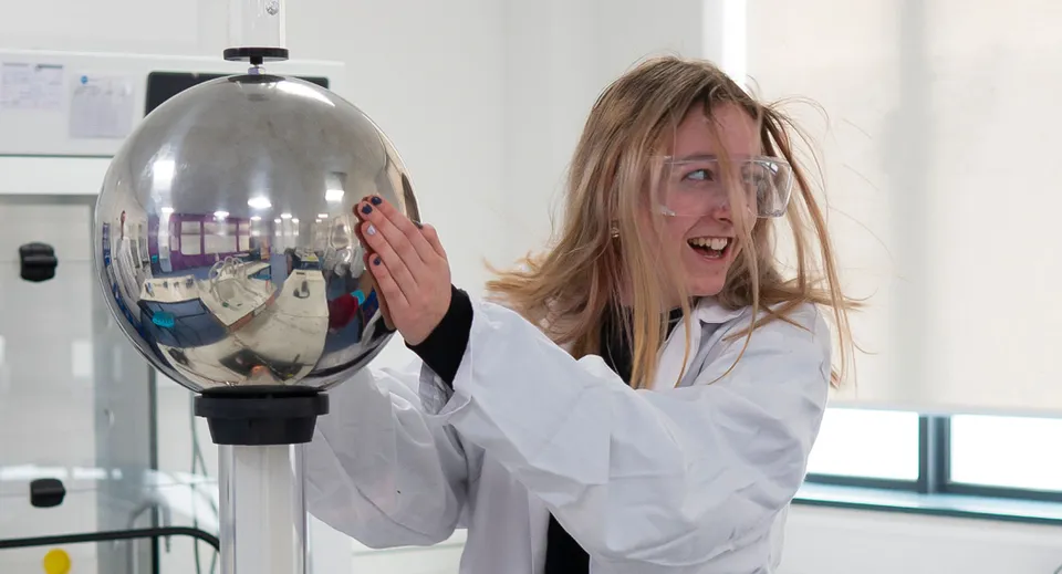 Una studentessa del Salisbury Sixth Form College esamina con entusiasmo un recipiente di vetro riflettente in laboratorio.