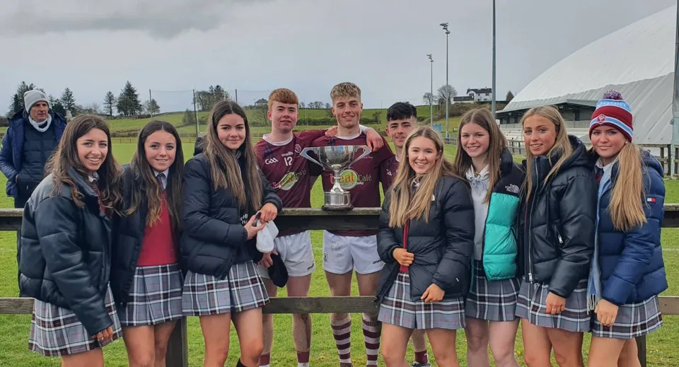 Un gruppo di studenti e studentesse della Mercy Secondary School tiene insieme un trofeo all'aperto nel campus scolastico.
