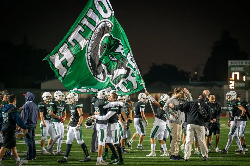 Giocatori di football americano della Torrance South High School festeggiano sul campo accanto a una grande bandiera verde.