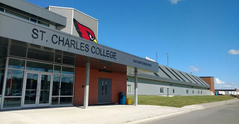 L'edificio moderno del St. Charles College con facciata in vetro e dettagli rossi davanti a un'area verde sotto un cielo blu.