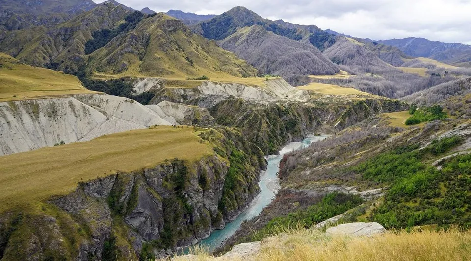 Sullo sfondo si vedono montagne innevate, davanti alle quali un fiume scorre attraverso il terreno roccioso nel campus della Kaiapoi High School.