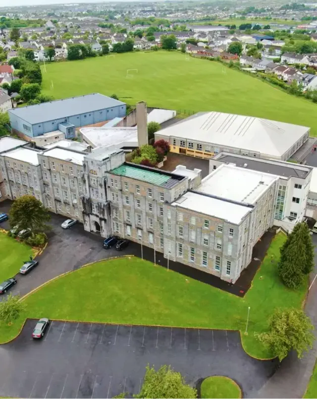 Veduta aerea di un campus scolastico irlandese con edificio storico, campi sportivi e case circostanti