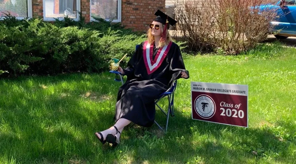 Una diplomata in toga sta davanti a un cartello con la scritta Class of 2020 sul campus della Marion M. Graham Collegiate.