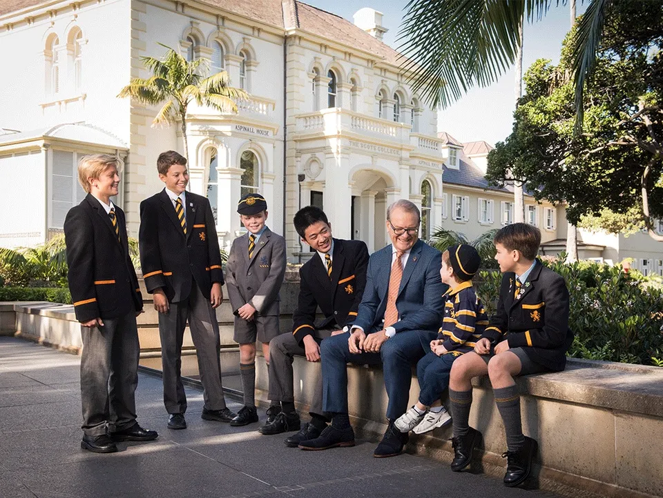 Un gruppo di studenti in divisa e un uomo in abito si trovano davanti al palazzo storico di The Scots College.