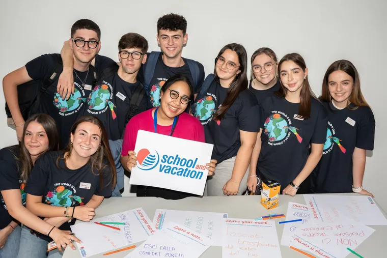 Gruppo di studenti sorridenti a un workshop mostra un cartello School and Vacation