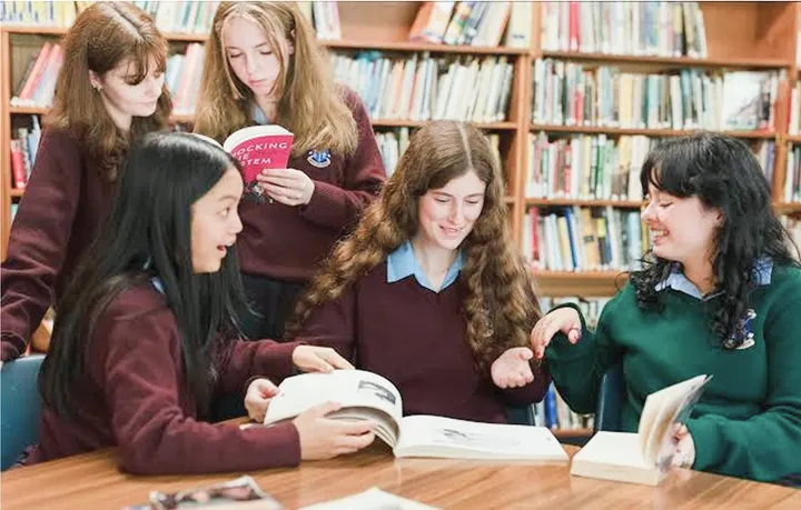 Estudiantes con uniforme leyendo libros en la biblioteca de la escuela
