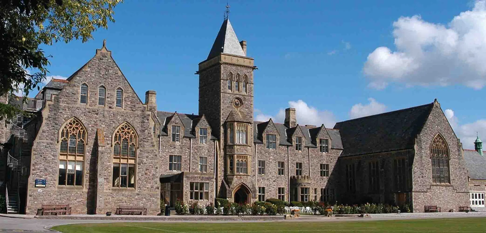 L'edificio medievale in pietra della Taunton School International è immerso nel verde e mostra persone in primo piano.