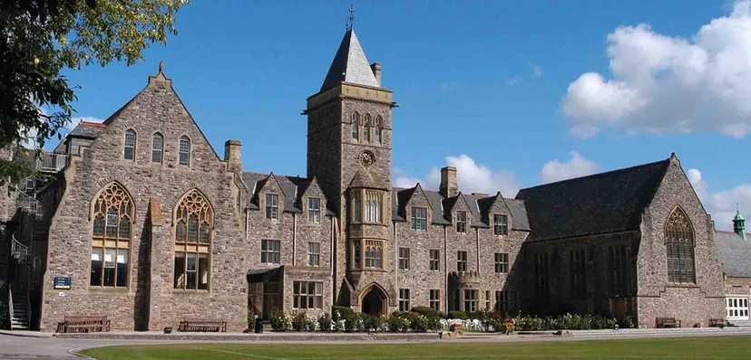 L'edificio medievale in pietra della Taunton School International è immerso nel verde e mostra persone in primo piano.