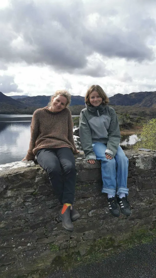 Dos personas sentadas en un muro de piedra ante un lago rodeado de montañas