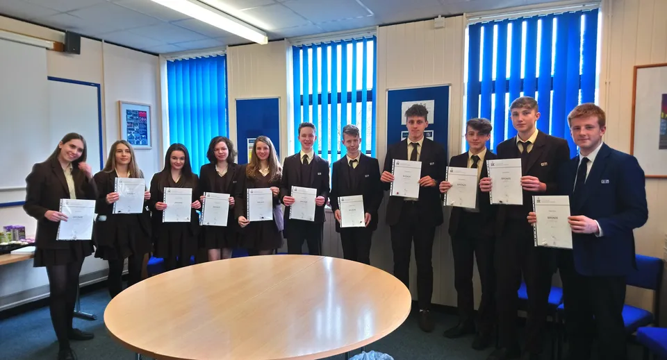 Studenti della Corfe Hills School in un'aula con veneziane blu mostrano i loro certificati.