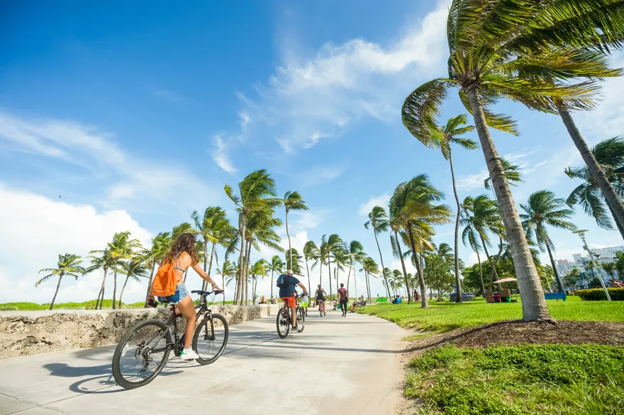 Jóvenes en bicicleta por un carril junto a la playa de Miami Beach entre palmeras