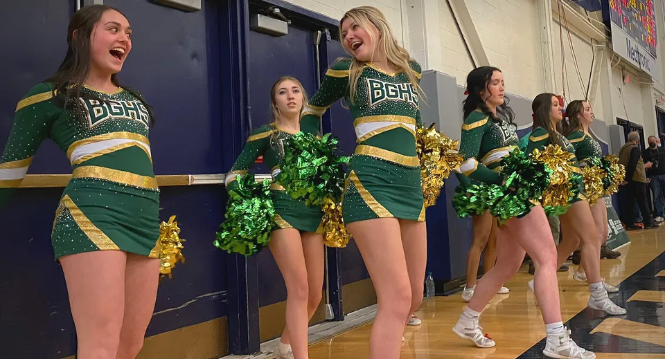 Un gruppo di cheerleader in uniformi verdi e dorate con i pompon nel corridoio della Bishop Guertin High School.