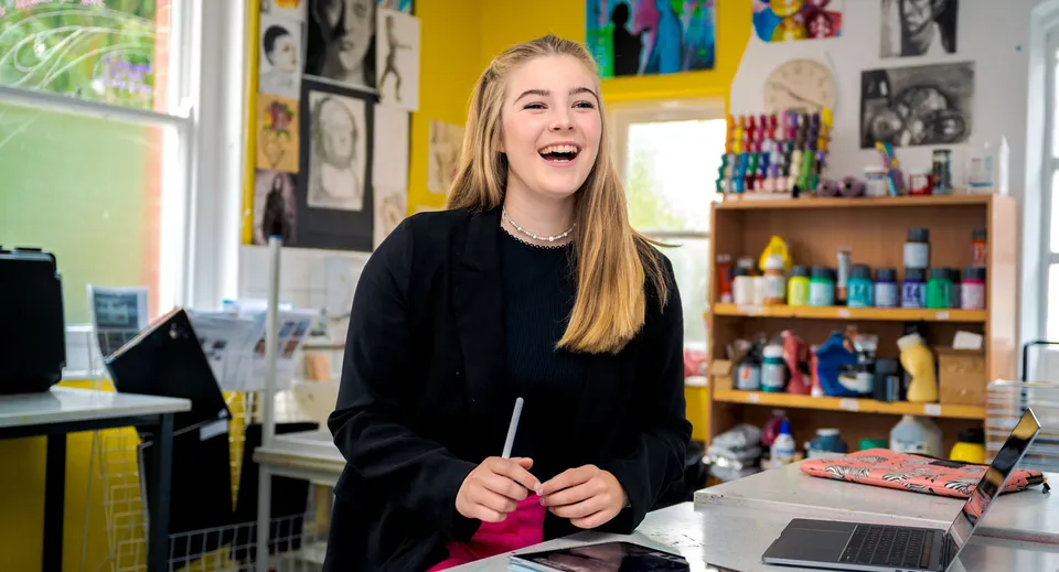 Una studentessa della Sherfield School siede sorridente in uno studio d'arte circondata da materiali artistici.