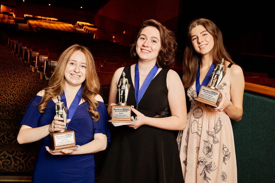 Tre studentesse della North Broward Preparatory School posano con dei premi davanti al sipario rosso dell'auditorium.