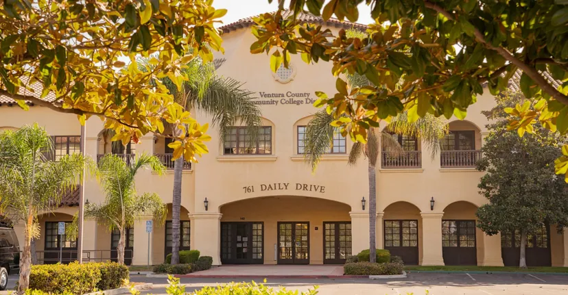 L'edificio in stile spagnolo nel campus del Ventura County Community College District è circondato da vegetazione verde e gialla.