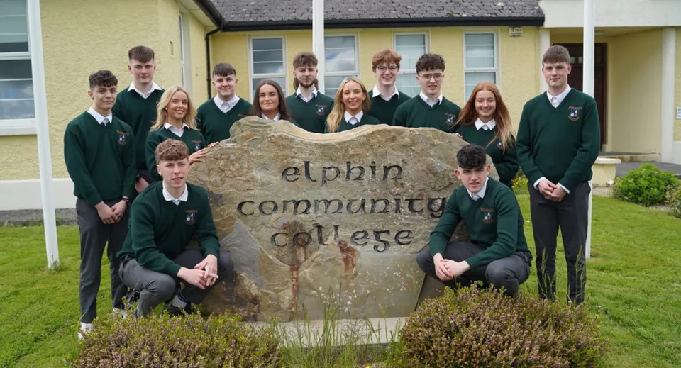 Un gruppo di studenti in divisa scolastica in posa davanti alla grande insegna in pietra dell'Elphin Community College.